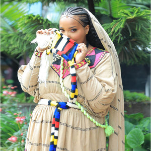 Woman wearing a colorful scarf and traditional outfit with a green, leafy background, shadey festival, habesha dress