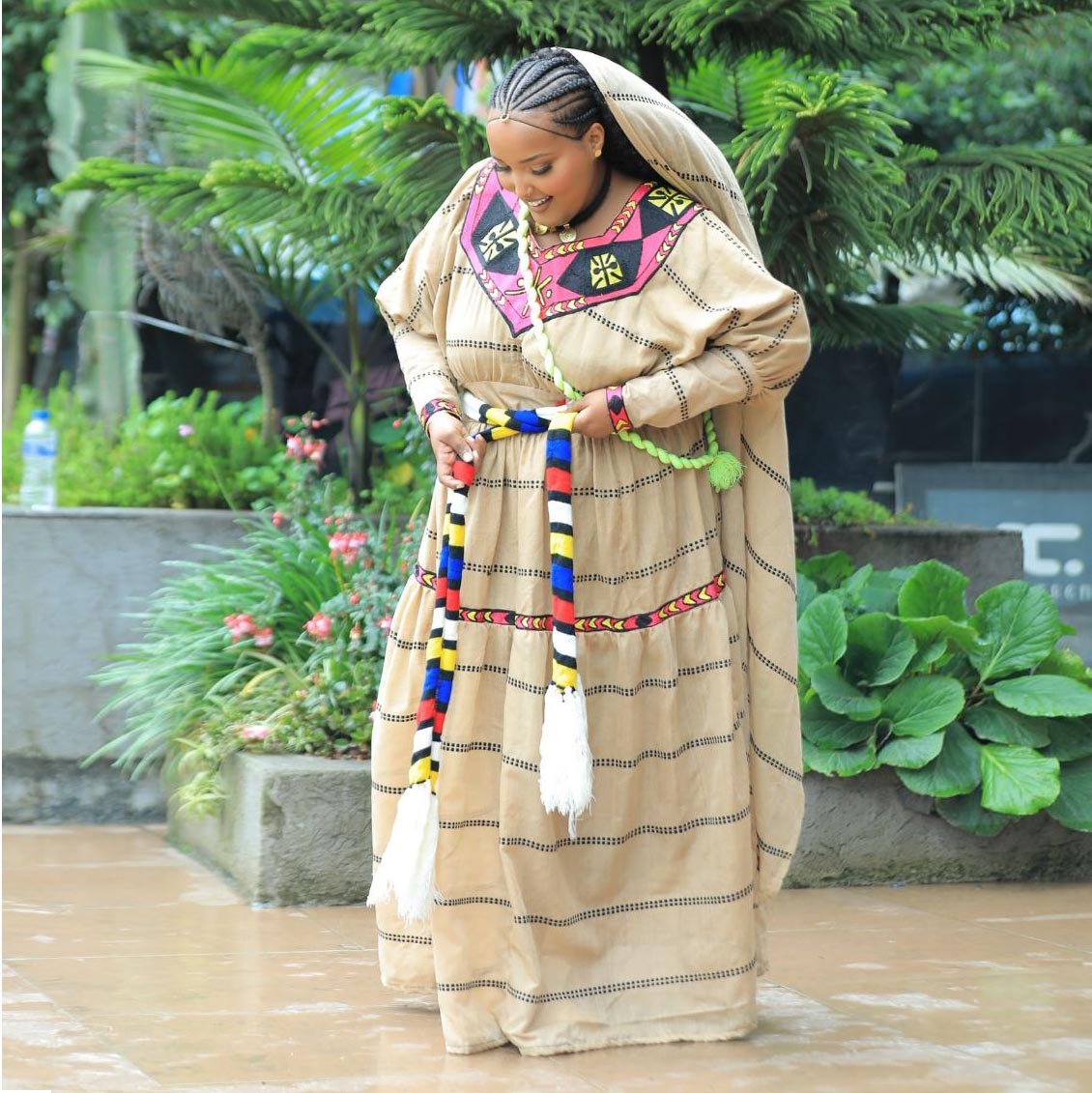 Woman in traditional attire with colorful accessories standing outdoors. Habesha kemis, Ayniwari Artistry